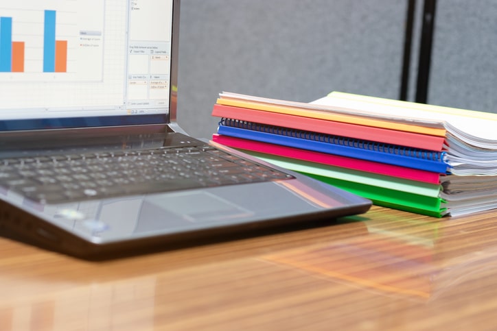 paperwork on a desk and a computer with bar graph report open