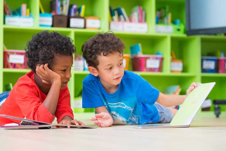 Two boys laying down reading a book in the library.