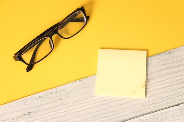 Glasses and post-it notes on desk with yellow background