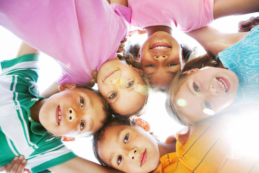 Below view of happy children embracing each other and smiling at camera