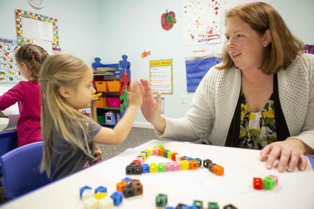 A child and teacher giving a high five after building a triangle together with blocks